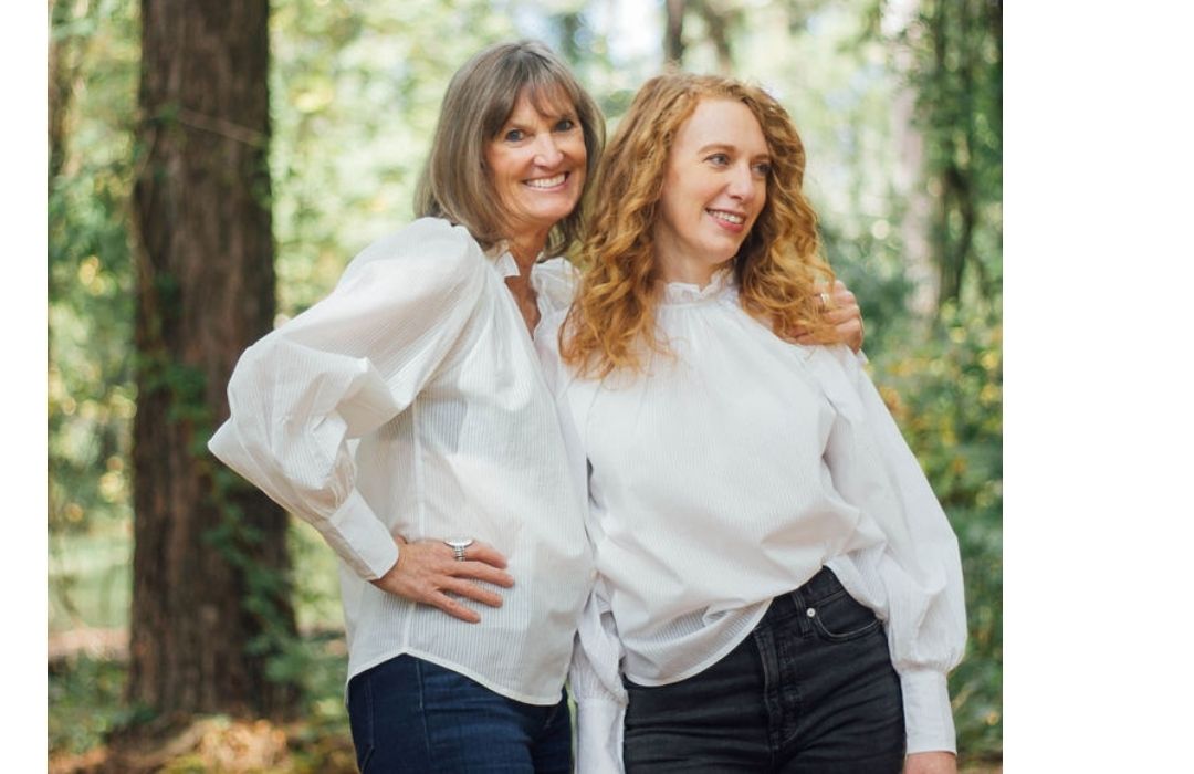 Two women wearing white blouses with billowed sleeves and ruffled collars. 